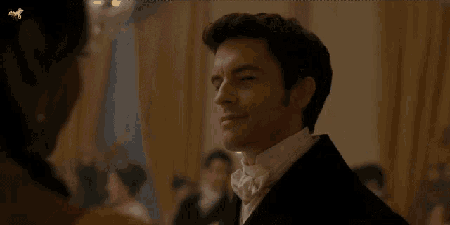 a man in a tuxedo and bow tie looks at a woman in a dress