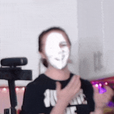a person with a white mask on their face is standing in front of a webcam .