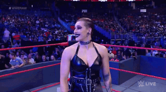 a woman in a black dress is standing in a wrestling ring with a crowd watching .