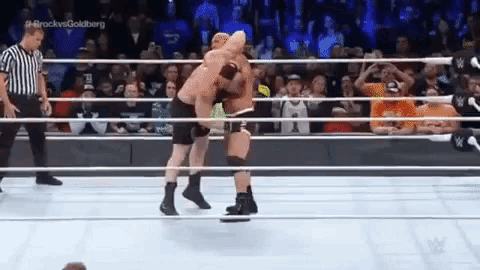 two men are wrestling in a ring while a referee watches .