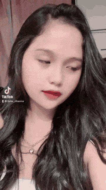 a woman with long black hair is wearing a white tank top and a necklace .