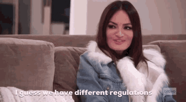 a woman is sitting on a couch wearing a denim jacket and a fur coat and talking .