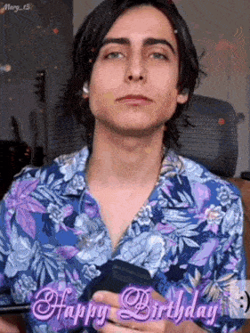 a young man in a floral shirt is holding a cell phone in his hand .