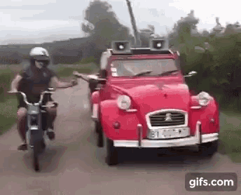 a man riding a motorcycle next to a red car on a road .