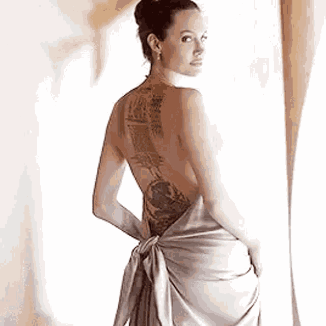 a woman with a tattoo on her back is wearing a dress and standing in front of a window .