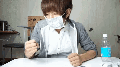 a man wearing a mask is sitting at a table with a bottle of water in front of him .