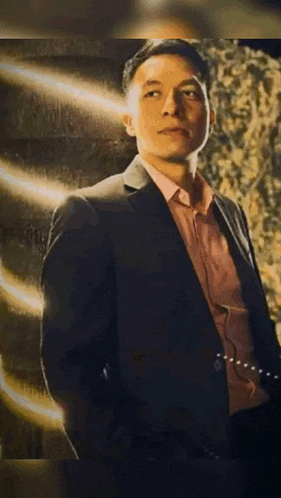 a man in a suit and red shirt is standing in front of a wall .