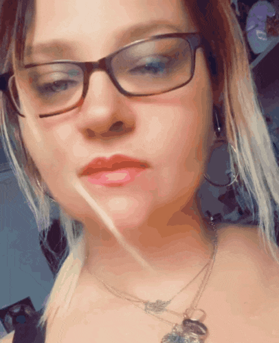 a woman wearing glasses and a necklace looks at the camera with her eyes closed