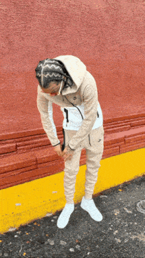 a man wearing a nike hoodie and sweatpants stands in front of a red wall