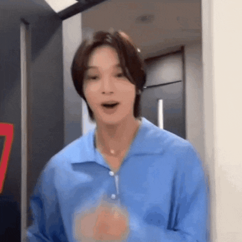 a young man in a blue shirt is standing in a doorway and making a funny face .