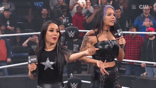 two women are standing in a wrestling ring holding microphones with a crowd behind them and a sign that says cw