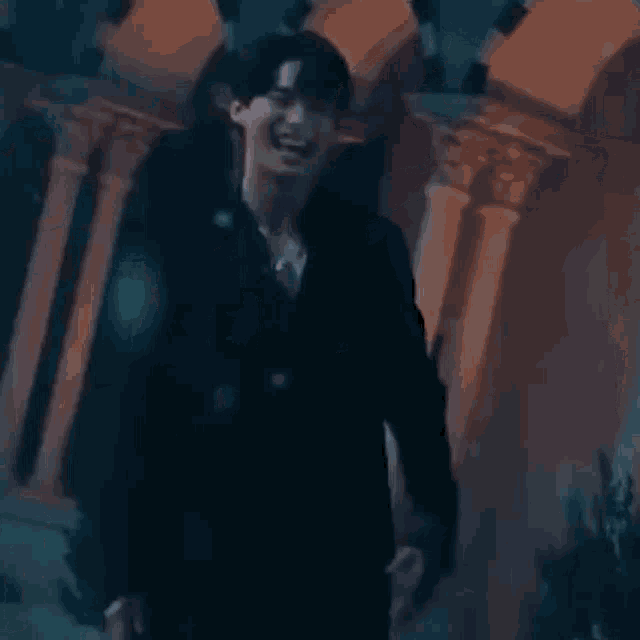 a man in a black suit is standing in front of a building with columns and smiling .