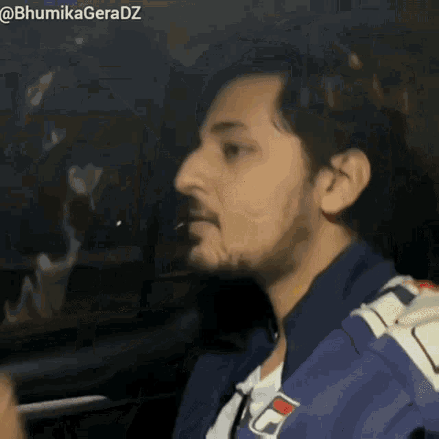 a man with a beard is sitting in a car with a fila jacket on .