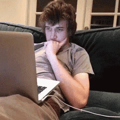 a young man is sitting on a couch looking at a laptop computer