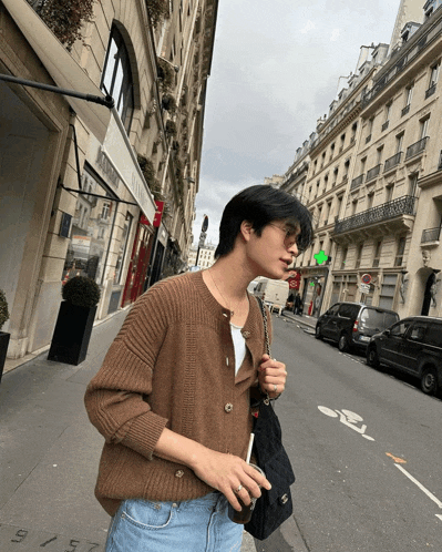 a man wearing a brown cardigan and jeans is walking down a street