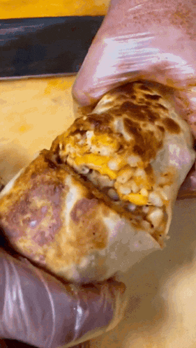 a person wearing gloves is holding a burrito on a table
