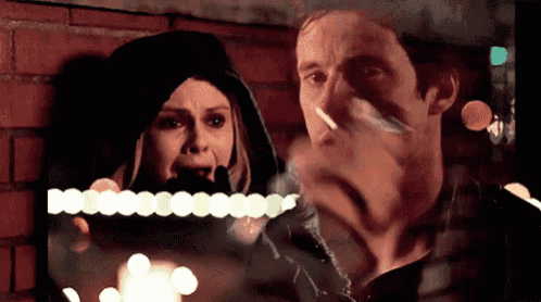 a man and a woman are standing next to each other and the man is smoking a cigarette