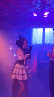 a girl in a pink and black dress is dancing in a dark room .