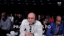a group of men are sitting in a stadium watching a boxing match and one of them is wearing headphones .