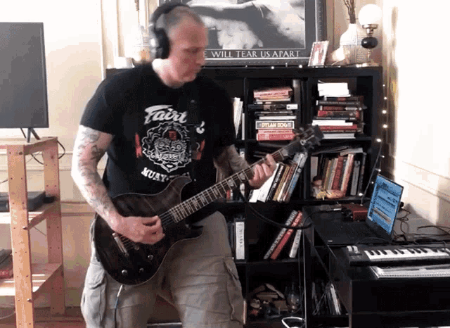a man is playing a guitar in front of a poster that says ' i will tear us apart '