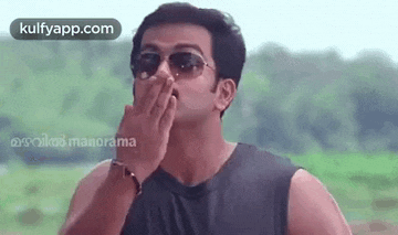 a man wearing sunglasses and a black tank top is blowing his nose .