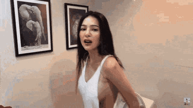 a woman in a white tank top is standing in front of two framed pictures of an elephant .