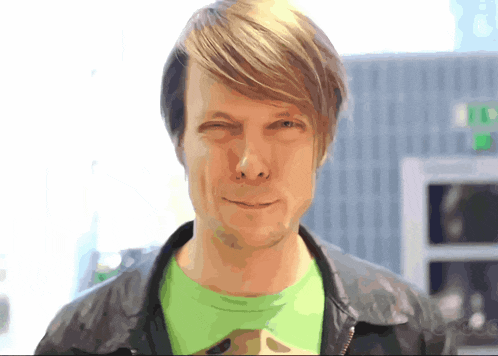 a man with a green shirt and a black jacket winks