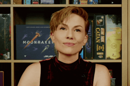 a woman stands in front of a shelf full of books including moonraker