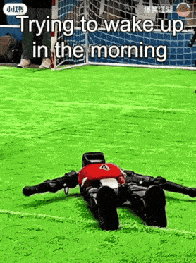 a robot is laying on a soccer field with the words trying to wake up in the morning below it