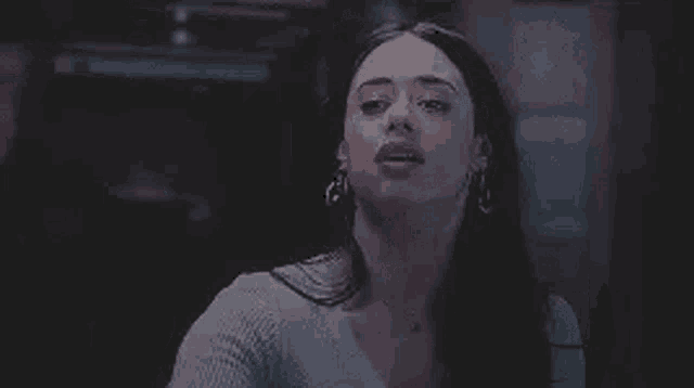 a woman with long black hair and earrings is making a funny face .