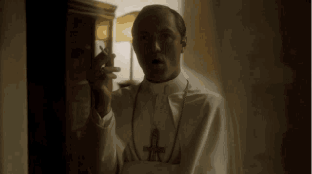 a priest is smoking a cigarette in a dark room .