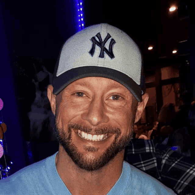 a man with a beard wears a ny hat