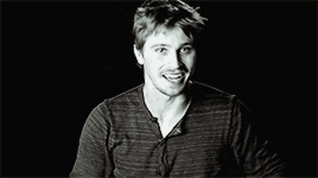 a black and white photo of a smiling man in a striped shirt .