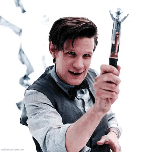 a man in a vest and bow tie holds a sonic screwdriver