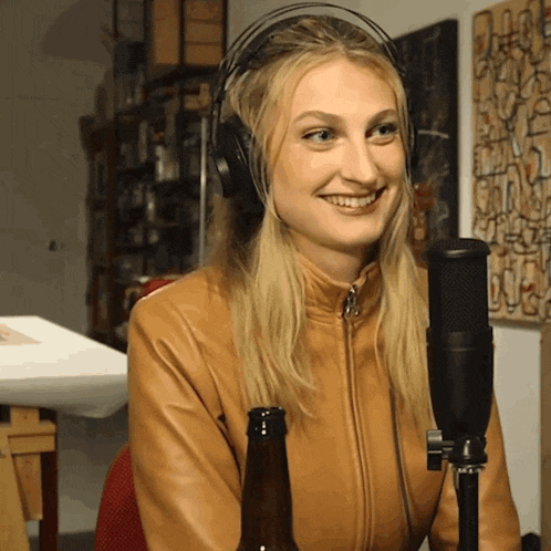a woman wearing headphones is smiling in front of a microphone and a bottle of beer