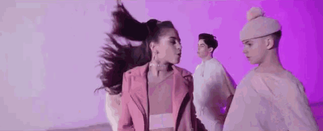 a woman in a pink jacket is dancing in front of a purple wall with two men .