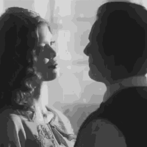 a black and white photo of a man and woman looking at each other .