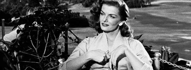 a black and white photo of a woman sitting on a bench with her hands folded .