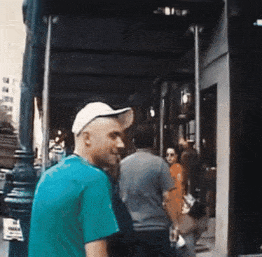 a man wearing a white hat and a blue shirt stands in front of a building