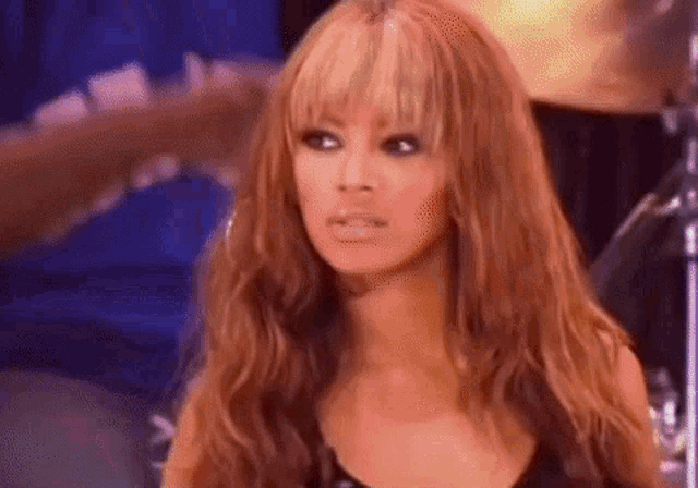 a woman with long red hair and bangs is standing in front of a drum set and making a funny face .