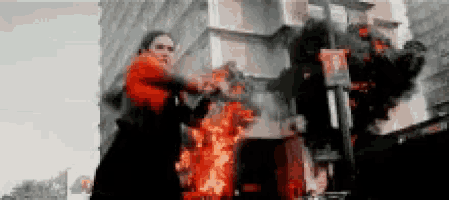a woman in a red dress is standing in front of a burning building .