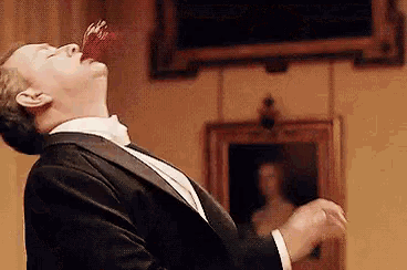 a man in a tuxedo is eating a piece of food with his mouth open .