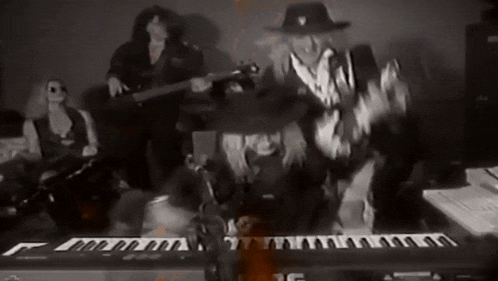 a black and white photo of a group of people playing instruments including a keyboard