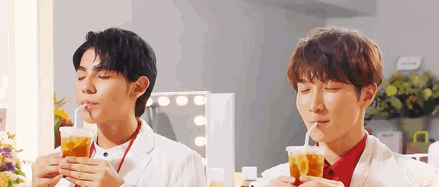 two young men are drinking through straws from plastic cups