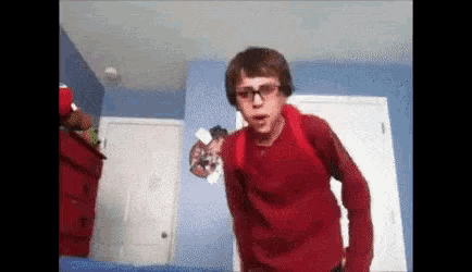 a young man wearing glasses and a red shirt is standing in a room .