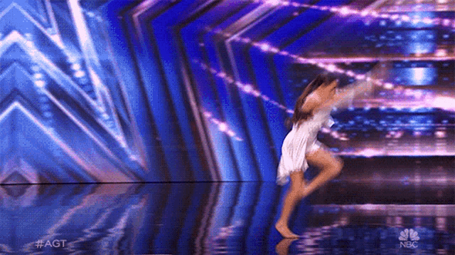 a woman in a white dress is dancing on a stage with a nbc logo in the corner