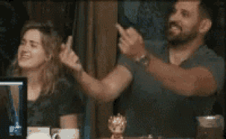 a man and a woman are sitting at a table with their hands up .