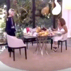 a woman sits at a table with a man standing behind her