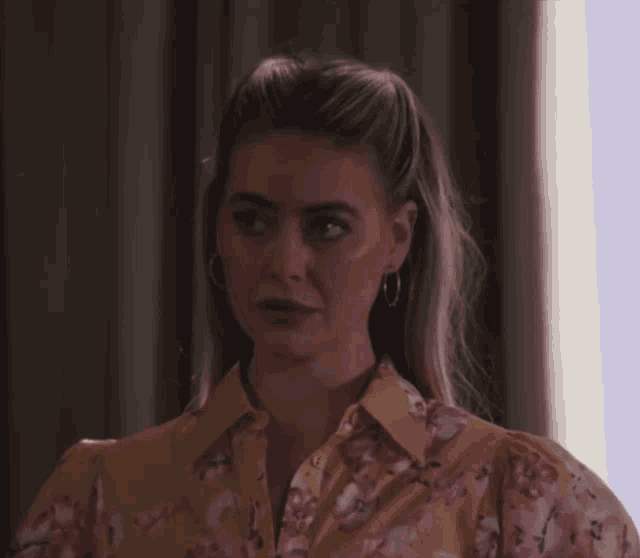 a woman wearing a yellow floral shirt and hoop earrings