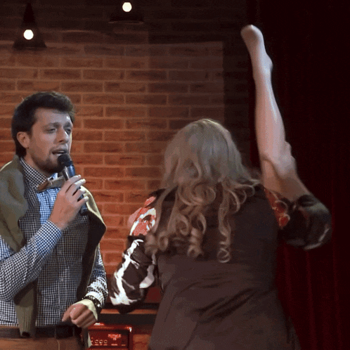a man singing into a microphone while a woman stands behind him